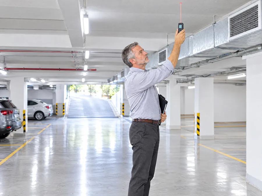 El Ingeniero de Estudio TREO mide con un medidor láser la altura de la cochera de un edificio, bajo los conductos de ventilación
